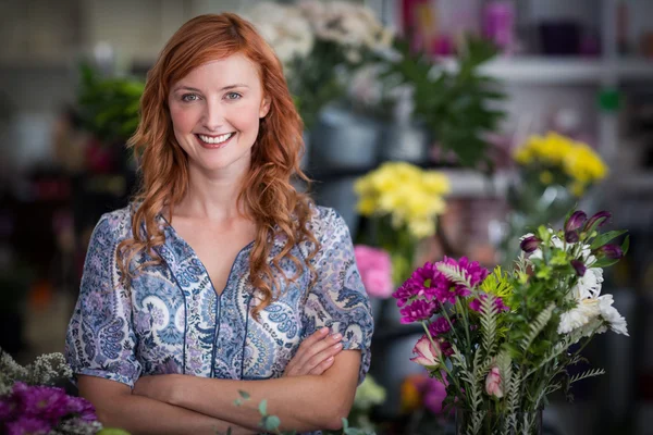 Щасливий жіночий флорист, що стоїть з гербами, схрещеними у квітковому магазині — стокове фото
