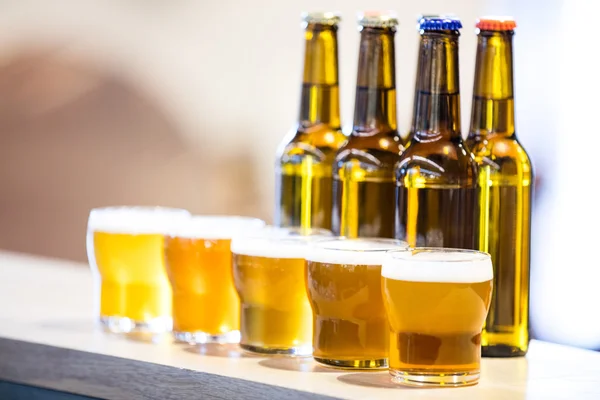 Copas de cerveza y botellas en el mostrador de la barra — Foto de Stock