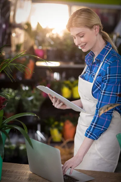 Kvinnelig blomsterhandler som bruker bærbar datamaskin mens hun holder skriveplate – stockfoto