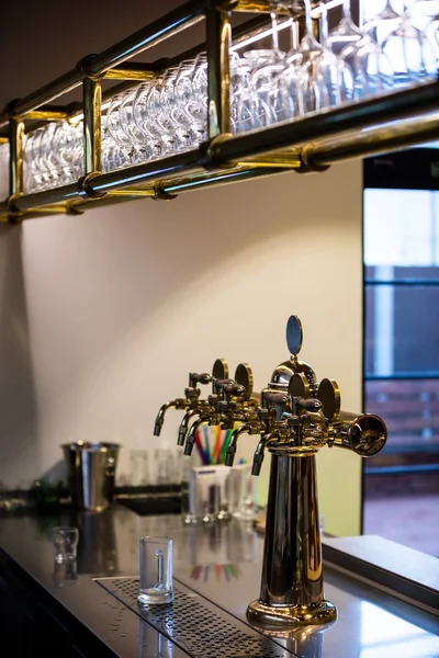 Empty glasses arranged on bar shelf and beer pump — Stock Photo, Image