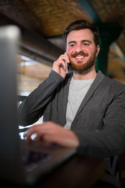 Adam cep telefonu üzerinde konuşurken ve dizüstü bilgisayar kullanarak — Stok fotoğraf