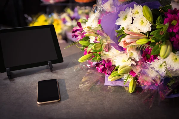 Ramo de flores con smartphone y tableta digital sobre la mesa —  Fotos de Stock