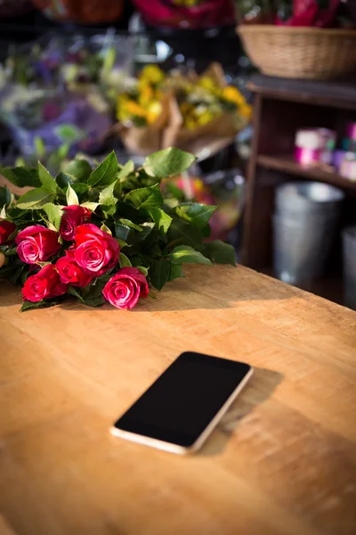 빨간 장미와 나무 테이블에 스마트폰 — 스톡 사진