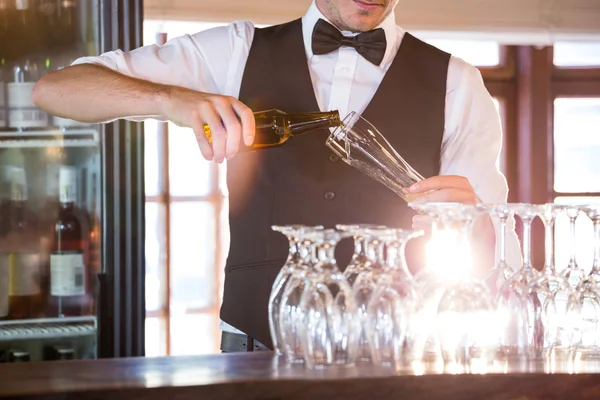 Seção intermediária do barman derramando uma cerveja em um copo — Fotografia de Stock