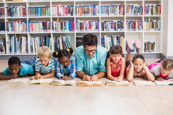 Professor e crianças lendo livro na biblioteca — Fotografia de Stock
