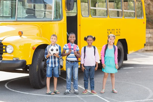 Улыбающиеся дети, стоящие вместе перед школьным автобусом — стоковое фото