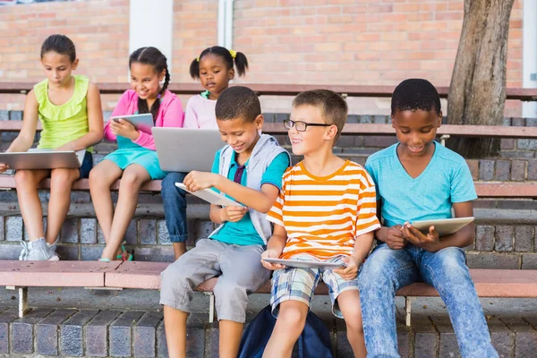 Enfants utilisant une tablette numérique et un ordinateur portable sur banc — Photo