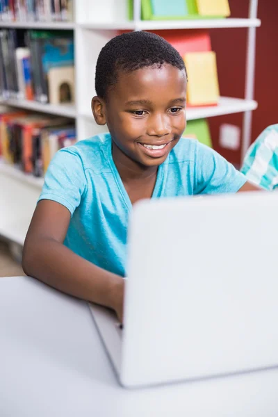 Schoolboy usando laptop na biblioteca — Fotografia de Stock