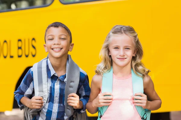 Niños sonrientes de pie frente al autobús escolar — Foto de Stock