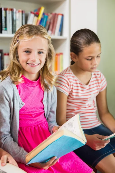 Schoolgirl reading a book in library — Stock Photo, Image
