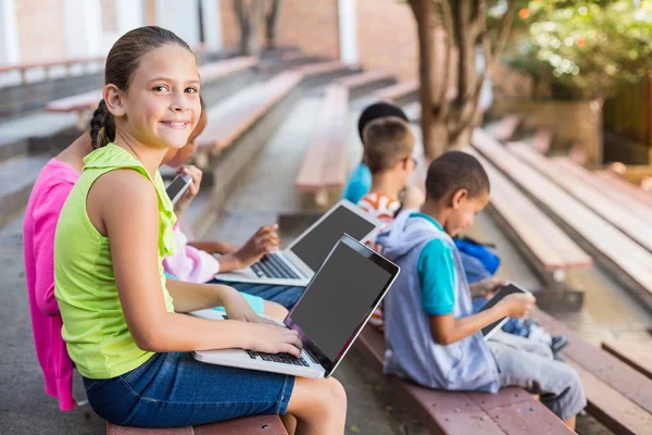 Дети сидят на скамейке и пользуются ноутбуком — стоковое фото