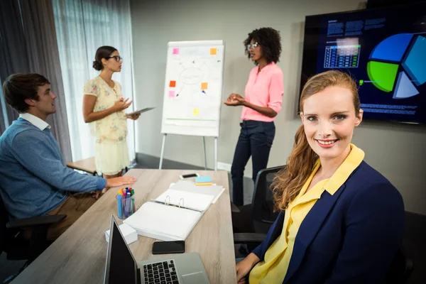 Kollega ler mot kameran medan medarbetare diskutera flödesschema — Stockfoto