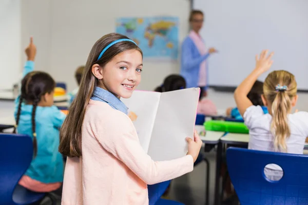 Porträtt av skolflicka stående med bok i klassrummet — Stockfoto