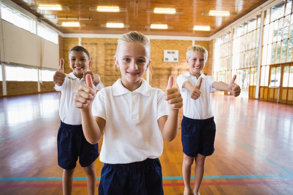 Estudiantes sonrientes mostrando pulgares arriba en el gimnasio de la escuela — Foto de Stock