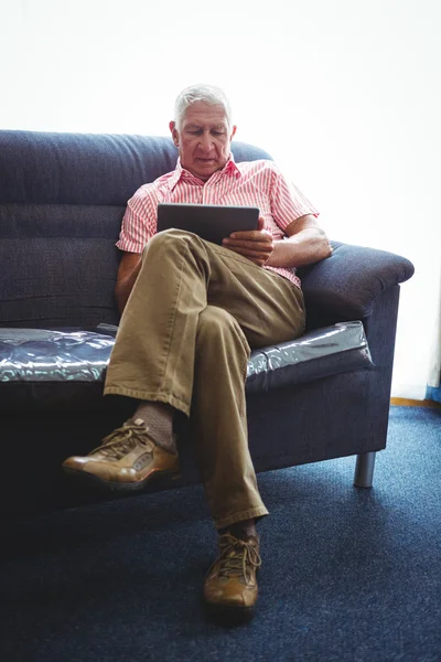 Starší muž, sedící na pohovce se zkříženýma nohama — Stock fotografie