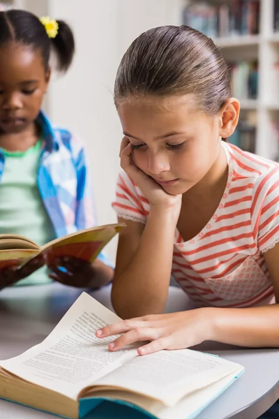 Skolflicka läser en bok i biblioteket — Stockfoto