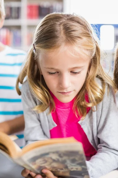 Schoolmeisje lezen van een boek in de bibliotheek — Stockfoto
