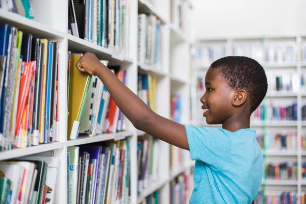 Schoolboy selecionando um livro de estante na biblioteca — Fotografia de Stock