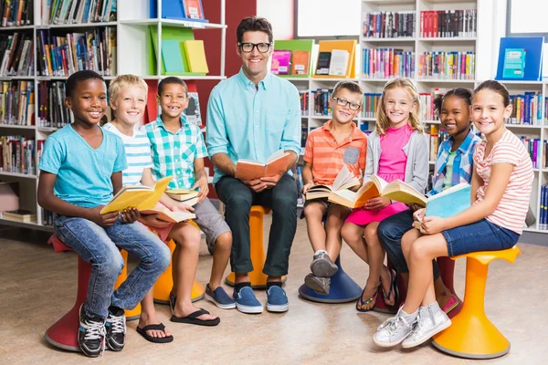 Professor e crianças sentados na biblioteca — Fotografia de Stock