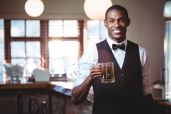 Barman sorridente oferecendo um copo de cerveja no balcão do bar — Fotografia de Stock