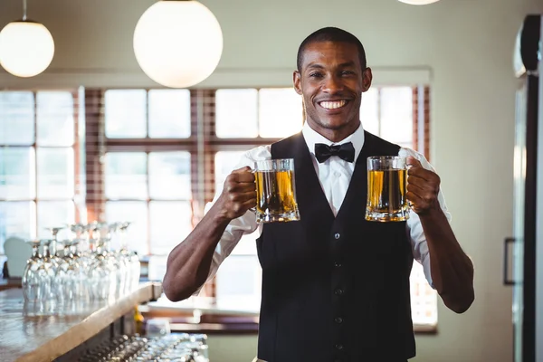 Lächelnder Barkeeper, der zwei Gläser Bier an der Theke anbietet — Stockfoto