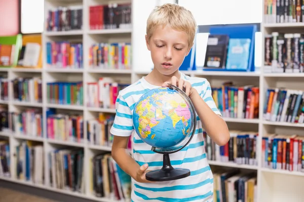 Schoolboy studying globe in library — Stock Photo, Image