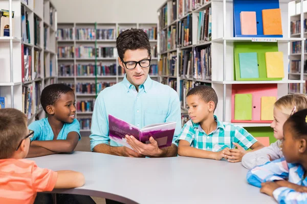 Professor e crianças lendo livro na biblioteca — Fotografia de Stock