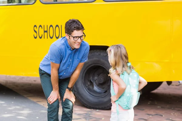 Enseignant et écolière interagissant devant le bus scolaire — Photo