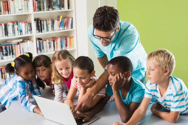 Professor e crianças usando laptop na biblioteca — Fotografia de Stock