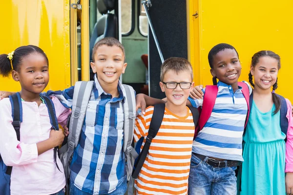 Smiling kids standing arm around in front of school bus — Stock Photo, Image