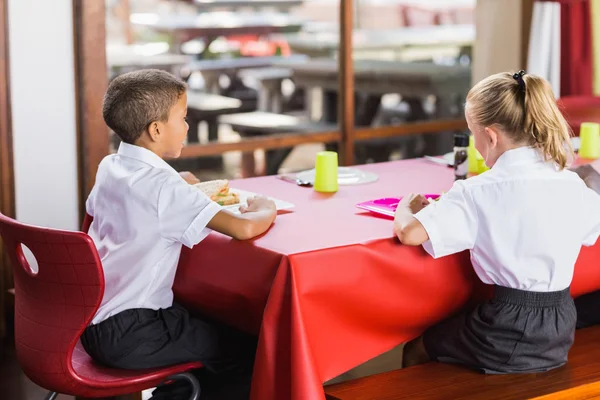 Menino e menina de uniforme escolar almoçando na cantina da escola — Fotografia de Stock