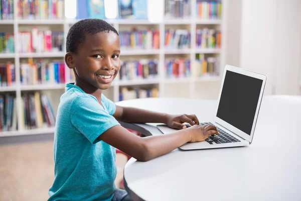Skolpojke med laptop i biblioteket — Stockfoto