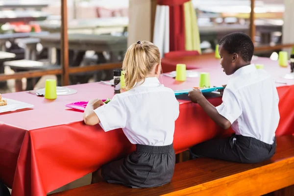 Boy and girl in school uniforms having lunch in school cafeteria — Stock Photo, Image