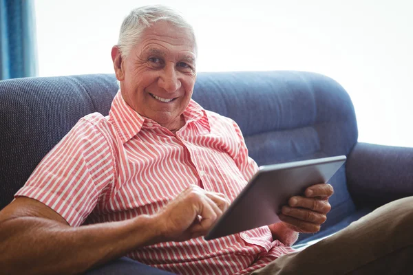 Äldre man sitter i en soffa titta på kameran — Stockfoto