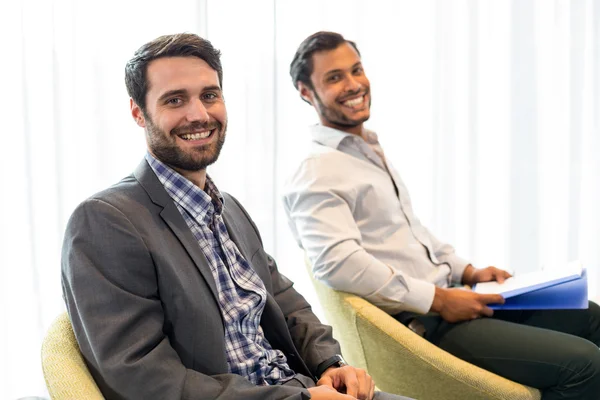 Homens sorrindo para a câmera enquanto sentados no escritório — Fotografia de Stock