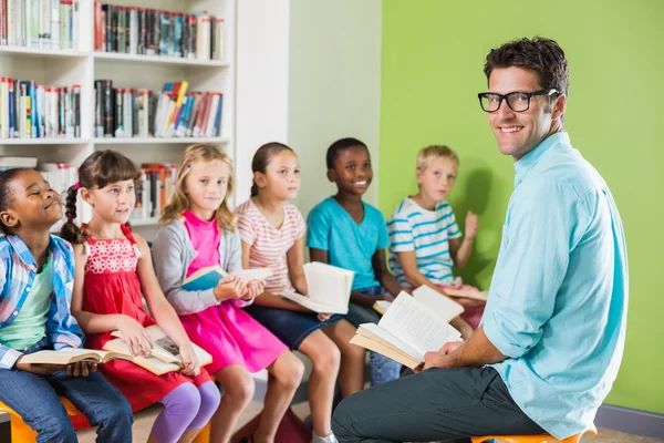 Вчитель і діти читають книгу в бібліотеці — стокове фото