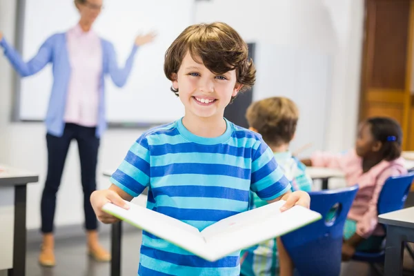 Portrait d'écolier debout avec livre en classe — Photo