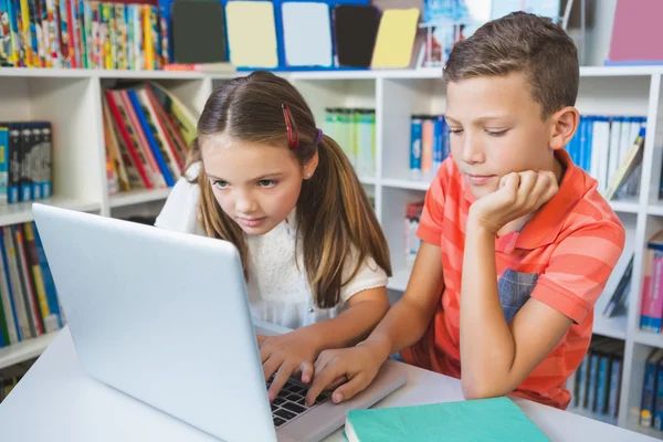 Crianças da escola usando um laptop na biblioteca — Fotografia de Stock
