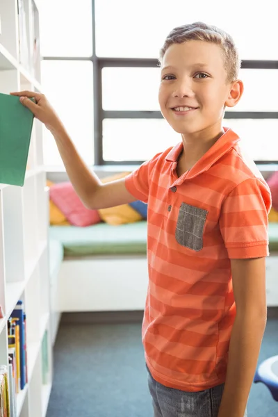 Jongen nemen van een boek uit de boekenkast in bibliotheek — Stockfoto