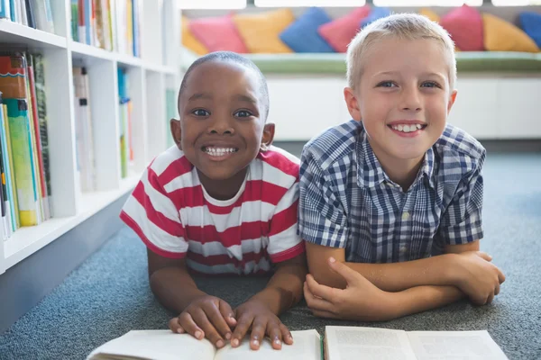 Retrato de niños de la escuela leyendo libro en la biblioteca — Foto de Stock