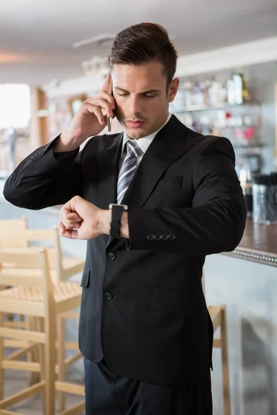 Empresario comprobando el tiempo mientras habla en el teléfono móvil — Foto de Stock