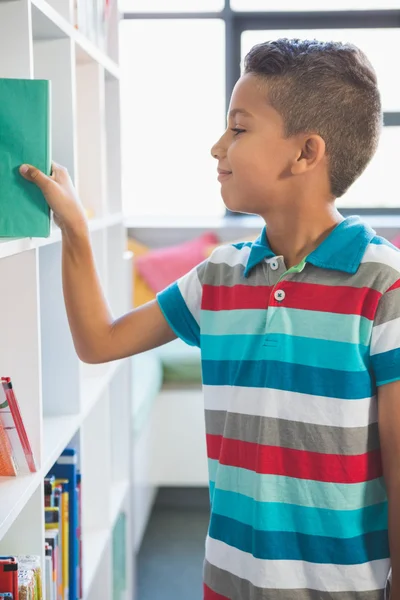 Jongen nemen van een boek uit de boekenkast in bibliotheek — Stockfoto