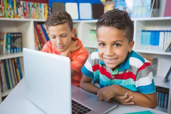 Niños de la escuela usando un portátil en la biblioteca — Foto de Stock