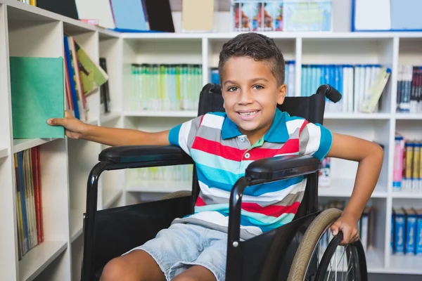 Menino com deficiência selecionando um livro de estante na biblioteca — Fotografia de Stock