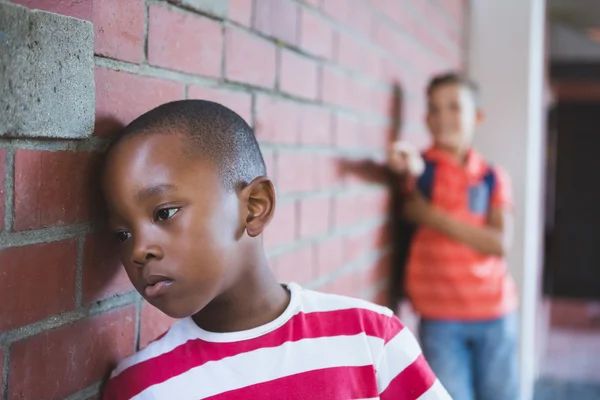 Un écolier intimide un garçon triste dans un couloir — Photo