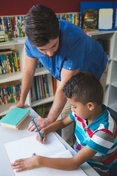 Leraar helpen school kind met zijn huiswerk in bibliotheek — Stockfoto