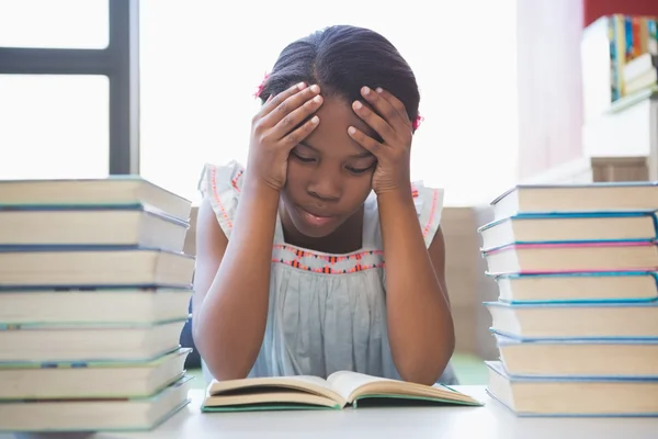 Escola menina lendo um livro na biblioteca — Fotografia de Stock