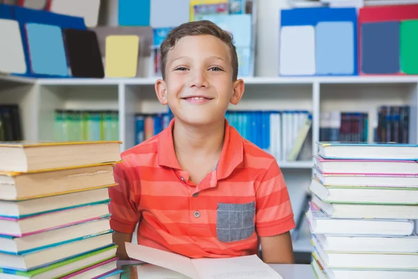 Schooljongen zittend op de tafel en lezing boek in bibliotheek — Stockfoto