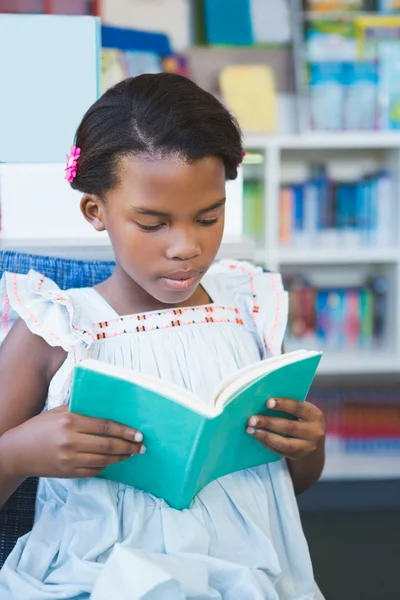 Schoolmeisje zittend op een stoel en lezing boek in bibliotheek — Stockfoto