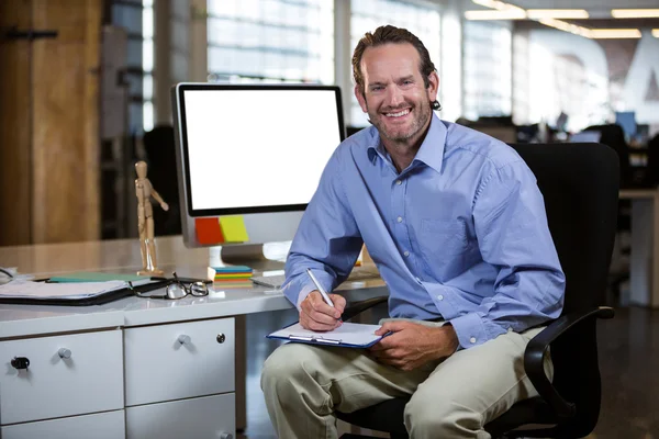 Businessman writing on clipboard by desk — Stock Photo, Image